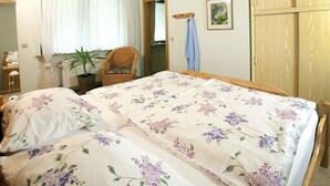 A bedroom with a wooden ceiling, a bed with floral bedding, a chair, a plant, and a wardrobe. - Inviting Apartment in Partschins/rabland (Enkirch)