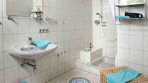 A bathroom with a sink, mirror, shower, and a small shelf with toiletries. - Inviting Apartment in Partschins/rabland (Enkirch)