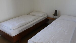 Ein Zimmer mit zwei Einzelbetten, jeweils mit weißer Bettwäsche. Dazwischen befindet sich ein kleiner Nachttisch.