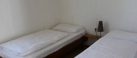 A room with two single beds, each with white bedding. There is a small wooden nightstand between the beds.