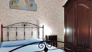 A bedroom with a bed, a wooden wardrobe, and a wall-mounted picture.