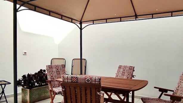 An outdoor patio with a table and chairs, a covered area, and a planter with plants.