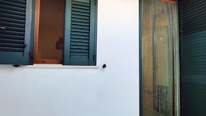 A building with a white exterior, a window with green shutters, and a green door with a mesh screen.