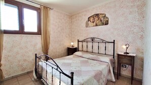 A bedroom with a bed, two bedside tables with lamps, a window with curtains, and a floral wallpaper. - Casa Marilda 2 - A 200 M dal Mare a Santa Maria Di Leuca (Castrignano del Capo)