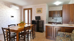A dining area with a table and chairs, a kitchen with wooden cabinets, a television, and a floral-patterned sofa. - Casa Marilda 2 - A 200 M dal Mare a Santa Maria Di Leuca (Castrignano del Capo)