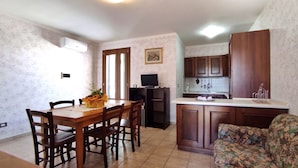 A compact kitchen with wooden cabinets, a dining table with chairs, a small TV, and a sofa. - Casa Marilda 2 - A 200 M dal Mare a Santa Maria Di Leuca (Castrignano del Capo)
