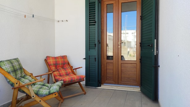 A balcony with two wooden chairs, a wooden door, and a view of buildings. - Casa Marilda 2 - A 200 M dal Mare a Santa Maria Di Leuca (Castrignano del Capo)