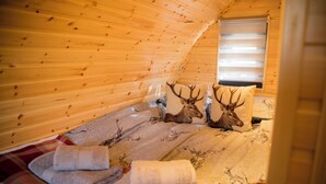 Una habitación acogedora con paredes de madera, una cama con una manta temática de ciervo y una ventana con persianas.