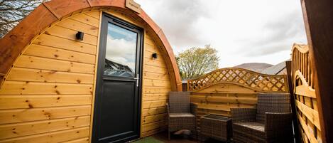 A wooden cabin with a curved roof, a black door, wicker furniture, and a wooden deck.