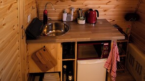 Cocina compacta con paredes de madera, un fregadero, un microondas y un refrigerador pequeño.