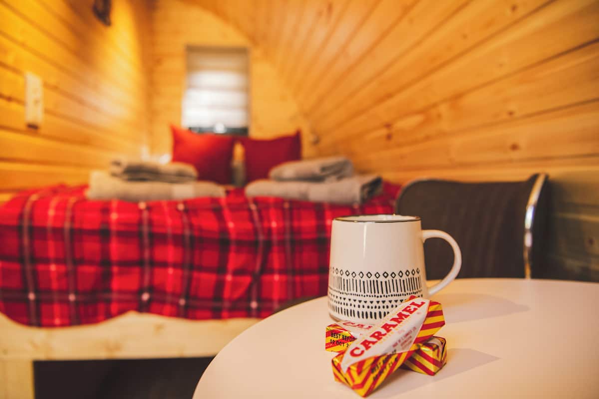 Una habitación de cabaña acogedora con una cama, una taza sobre una mesa y una manta escocesa roja.
