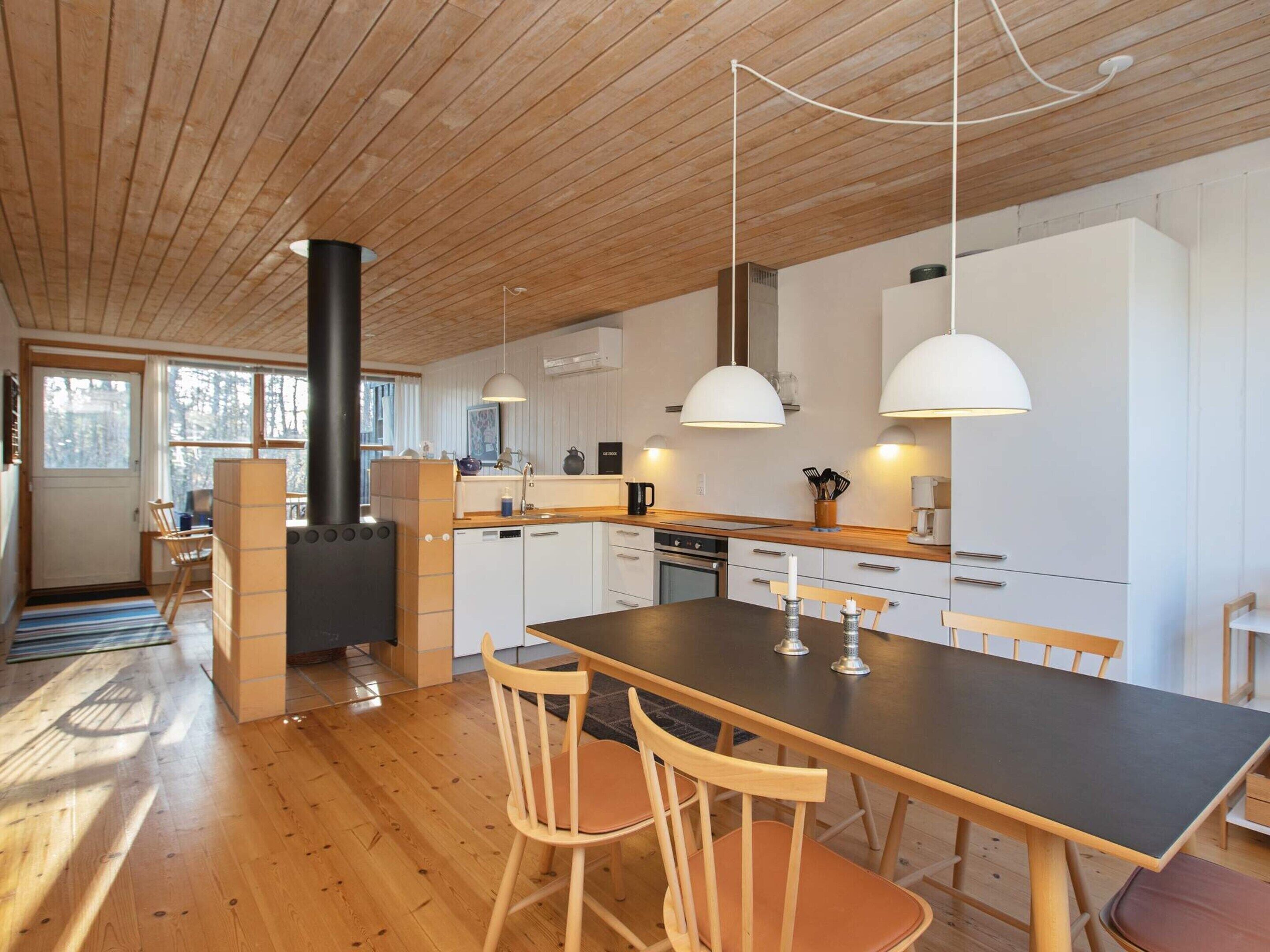 A modern kitchen with wooden floors, a central island, pendant lights, and a built-in stove.