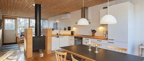 A modern kitchen with wooden floors, a central island, pendant lights, and a built-in stove.