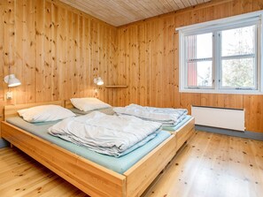 Une pièce aux murs lambrissés, avec deux lits, une fenêtre et un radiateur.
