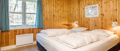 A wooden-paneled bedroom with a bed, two bedside lamps, a window with curtains, and a radiator.