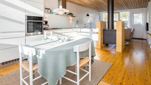 Une cuisine moderne avec des meubles blancs, un îlot central doté de sièges, une cuisinière encastrée et un coin repas avec une table et des chaises.