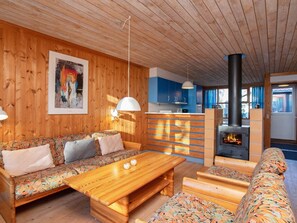 A cozy cabin interior with wooden walls, a sofa, a wooden table, and a fireplace. - 4 Person Holiday Park Home in Vaeggerlose (Vaeggerlose)