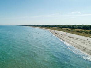 Ein Strand mit klarem Wasser, sandigem Ufer und bewaldetem Hintergrund.