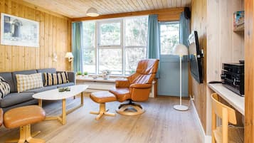 Una sala de estar acogedora con paredes de madera, un sofá, un sillón de cuero, una mesa de centro y un televisor.