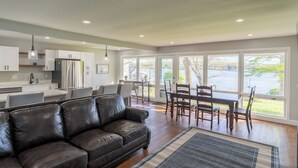 A spacious living area with a dark leather sofa, a dining table with chairs, and a kitchen area with white cabinets and a refrigerator. - Stunning Lakeside Retreat (Columbia)