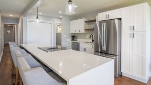 A modern kitchen with white cabinetry, stainless steel appliances, and a long island with bar stools. - Stunning Lakeside Retreat (Columbia)