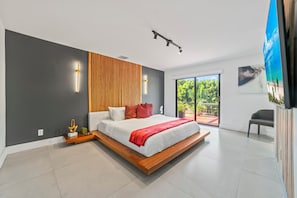 A modern bedroom with a large bed, a wooden headboard, and a view of greenery outside.