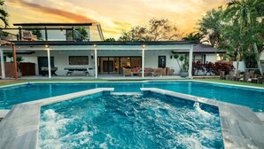 Une maison moderne dotée d’une piscine, d’un patio couvert et offrant une vue sur le coucher de soleil.