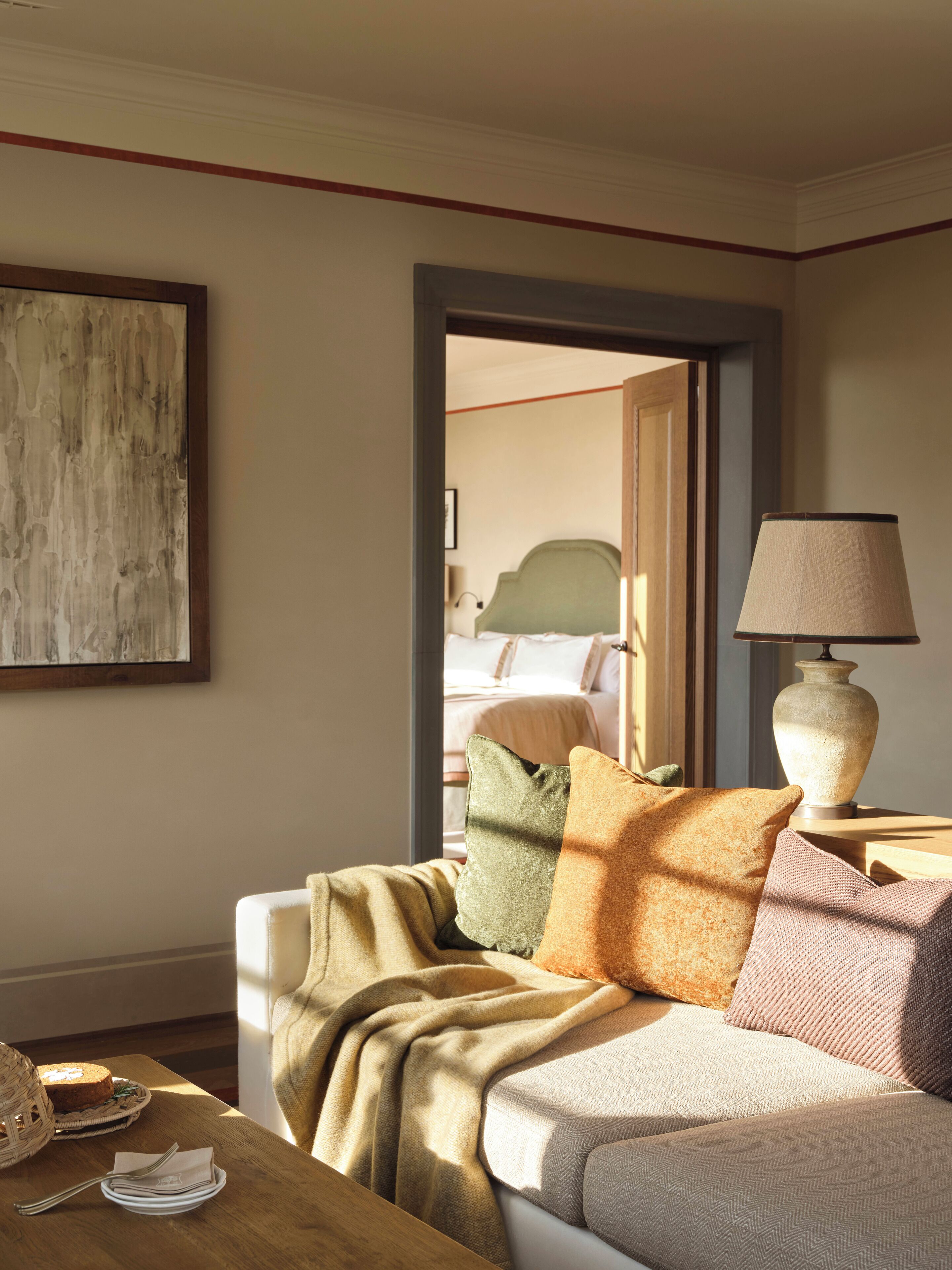 A cozy room with a bed, a table with a lamp, and a painting on the wall.