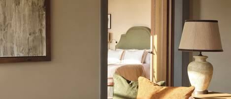 A cozy room with a bed, a table with a lamp, and a painting on the wall.