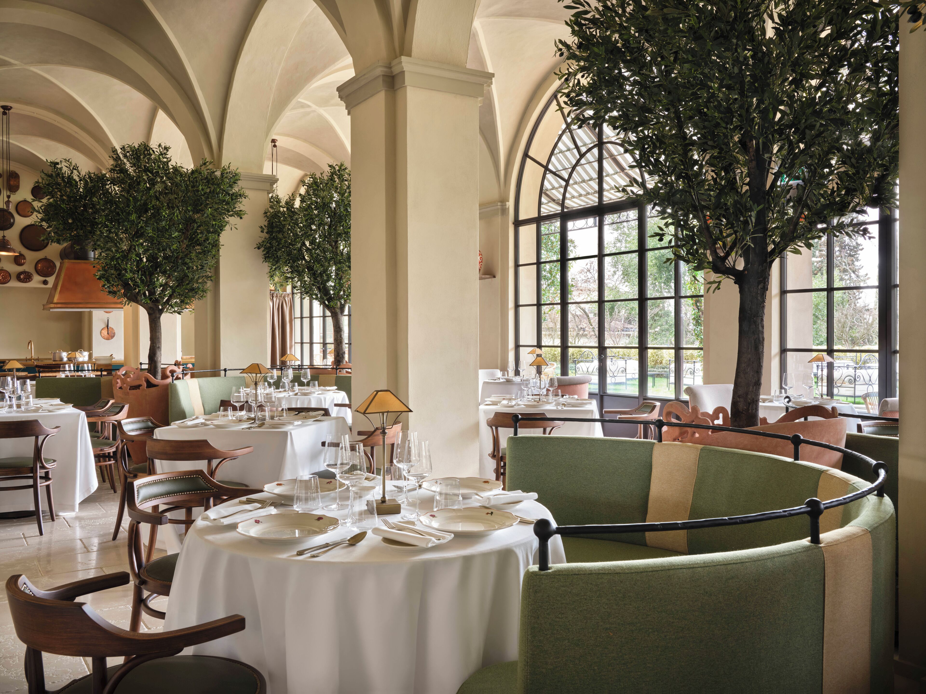 A restaurant with round tables, green upholstered chairs, and large windows.