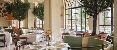 A restaurant with round tables, green upholstered chairs, and large windows.