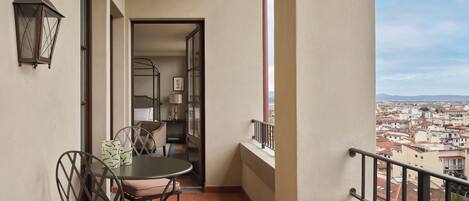 Un balcón con mesa y sillas, vista a la ciudad y una puerta que da a un dormitorio.