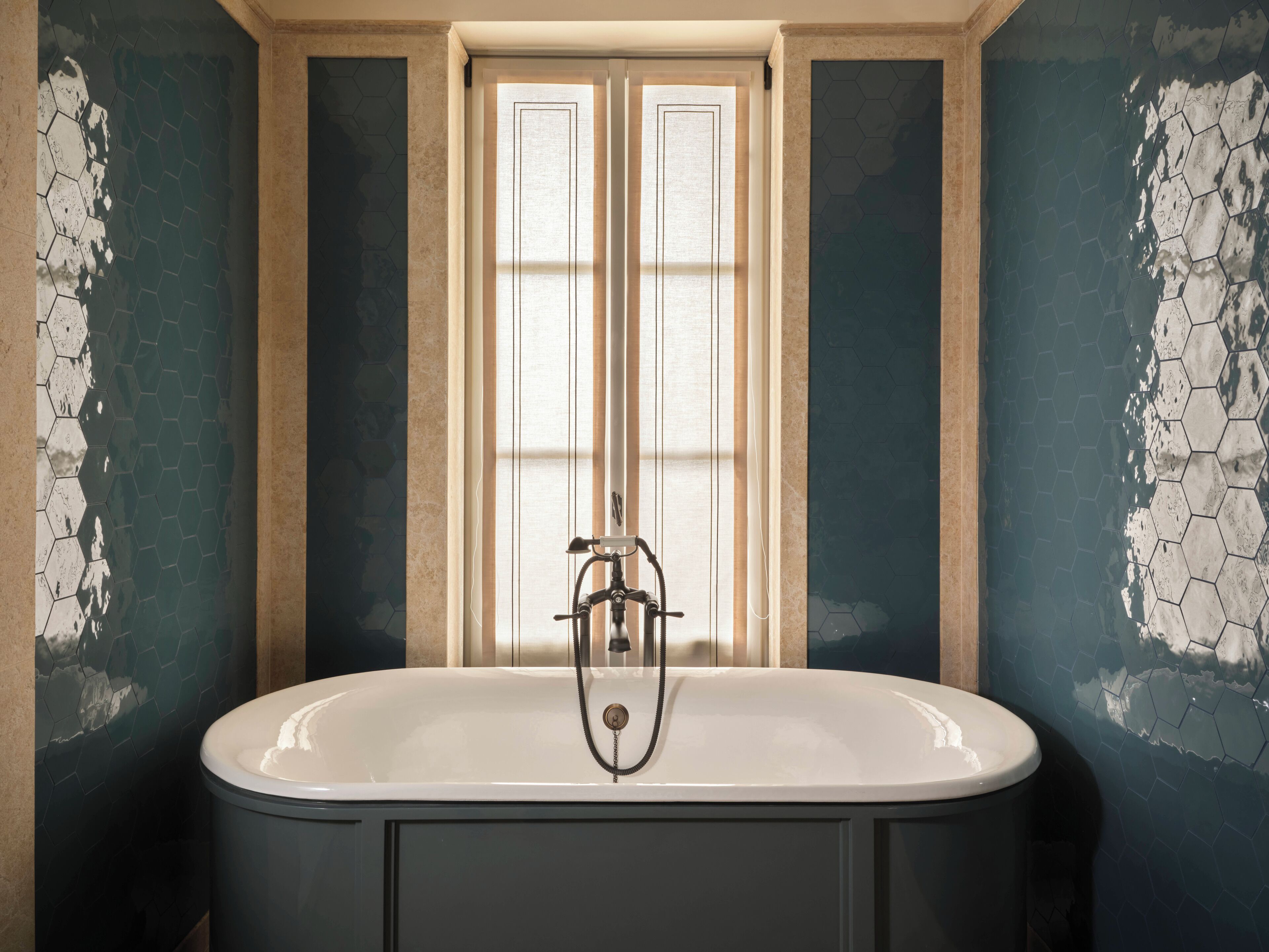Un bagno con una vasca freestanding, una finestra con vetro satinato e pareti con motivo esagonale.
