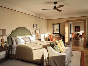 Quarto com cama, sofá, escrivaninha e cadeira. Há um ventilador de teto sobre a cama.