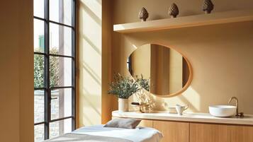 Un baño moderno con un ventanal grande, un espejo redondo, un lavabo blanco y un mueble de tocador de madera.