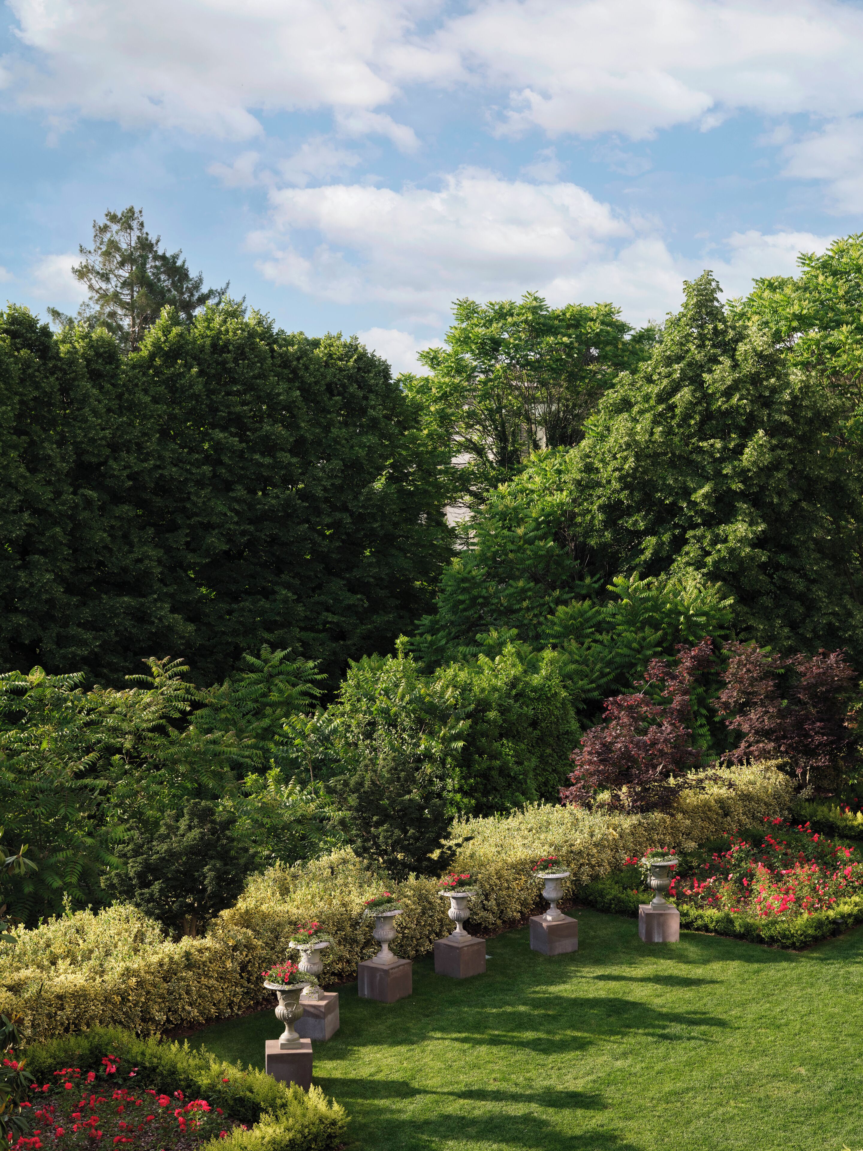 Un jardin bien entretenu, agrémenté de diverses plantes et arbres, de jardinières en pierre et d’un ciel dégagé.