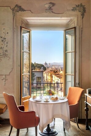 A dining area with a table set for two, a view of a cityscape through open windows, and a balcony with a railing. - Collegio alla Querce, Auberge Collection (Florence)