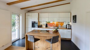 Una cocina moderna con vigas de madera, armarios blancos, una isla central con taburetes altos y un ventanal grande.
