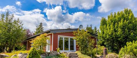 A red house with a satellite dish, surrounded by lush greenery and a clear blue sky.