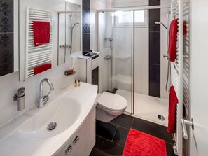 Ein modernes Badezimmer mit einem weißen Waschbecken, einer Toilette, einer Duschkabine und einem roten Handtuch auf dem Handtuchhalter.