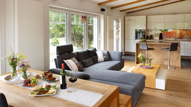 Un salón moderno con un sofá gris, una mesa de comedor de madera y una cocina al fondo.