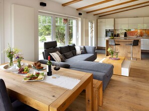 Ein modernes Wohnzimmer mit grauem Sofa, Holzesstisch und einer Küche im Hintergrund.