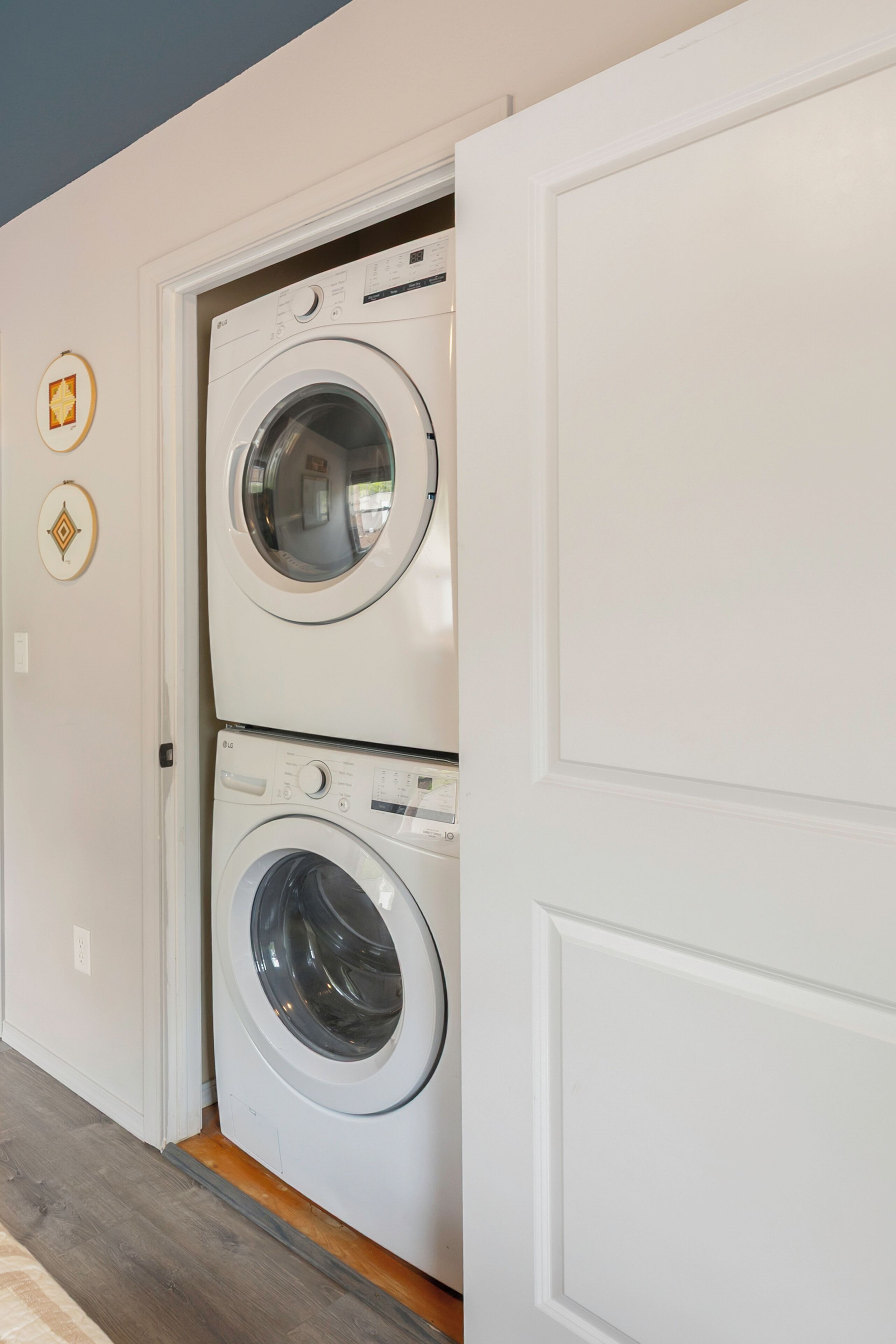 A laundry room with two stacked front-loading washing machines, a wooden floor, and a white door.