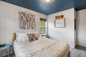 A bedroom with a bed, a wall art piece, a window, and a sign on the wall.