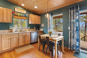 A kitchen with wooden cabinets, a dining table with chairs, a hanging light fixture, and a view through a window.