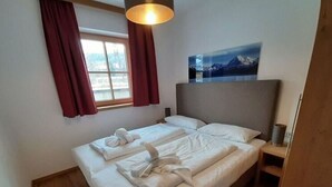 A hotel room with a bed, a painting on the wall, and a window with curtains. - Alpin Residenzen Top 12 (Hollersbach im Pinzgau)
