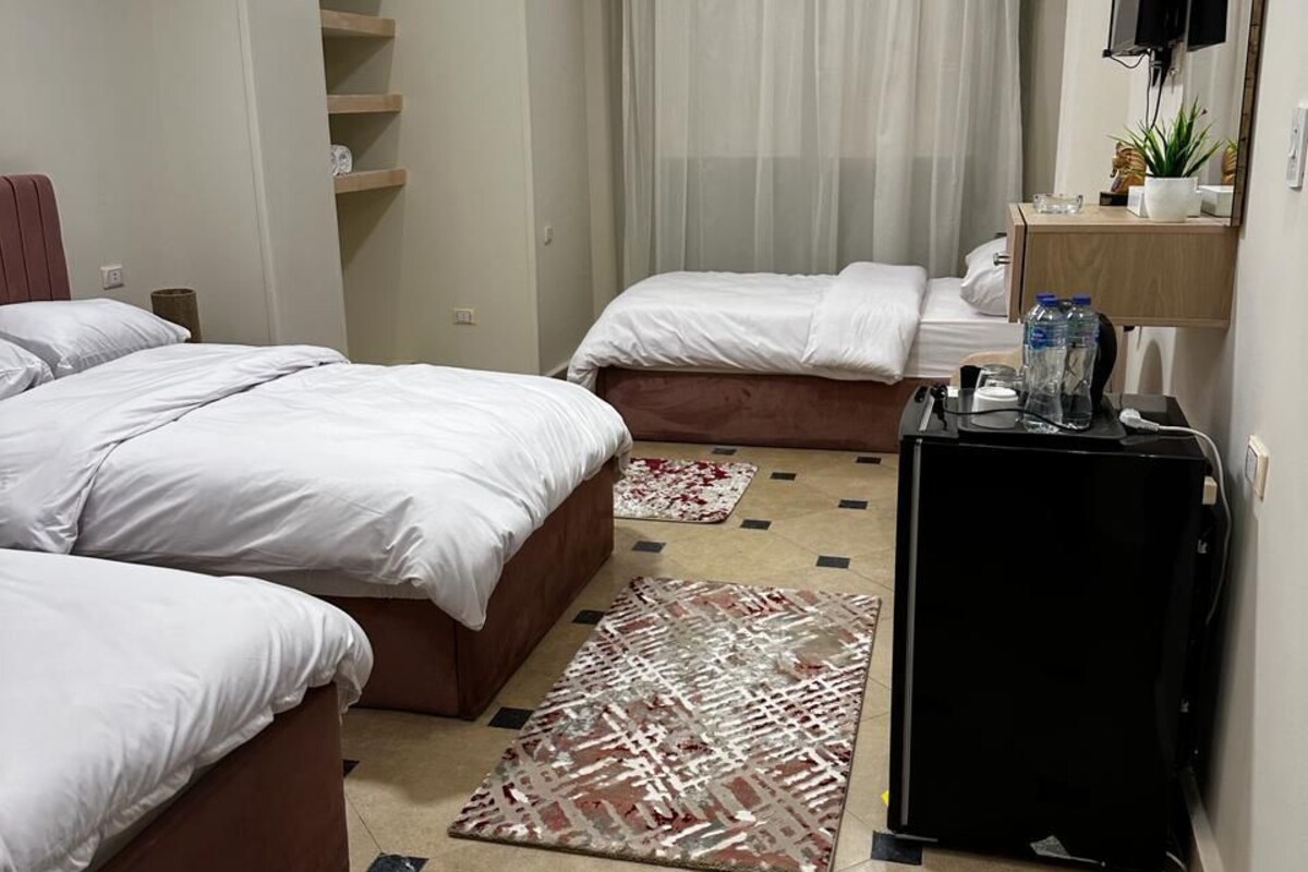 Une chambre d’hôtel avec deux lits, un bureau avec un ordinateur, une télévision et une petite étagère avec des articles de toilette.