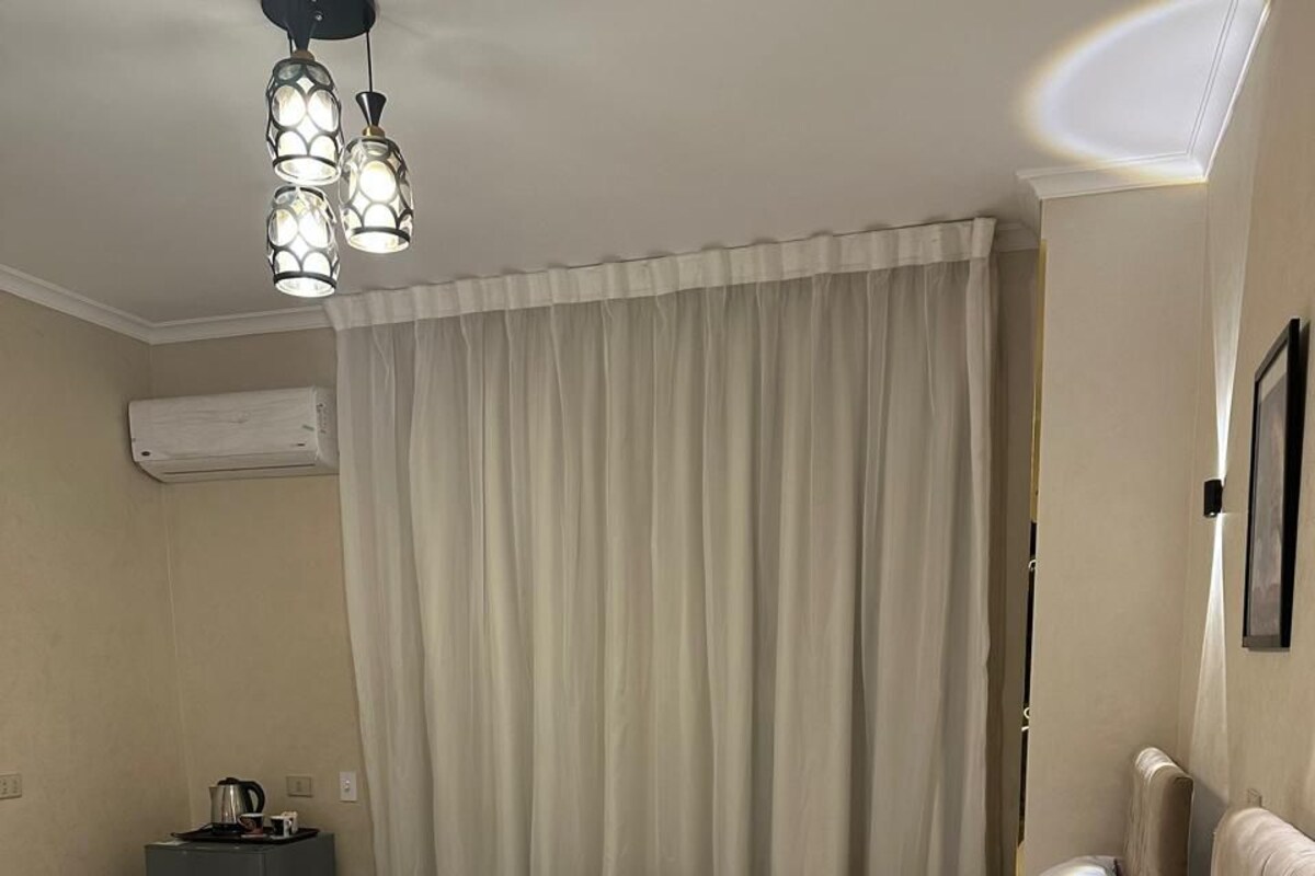 Une chambre d’hôtel avec deux lits, une petite table avec une bouilloire et un luminaire au plafond.
