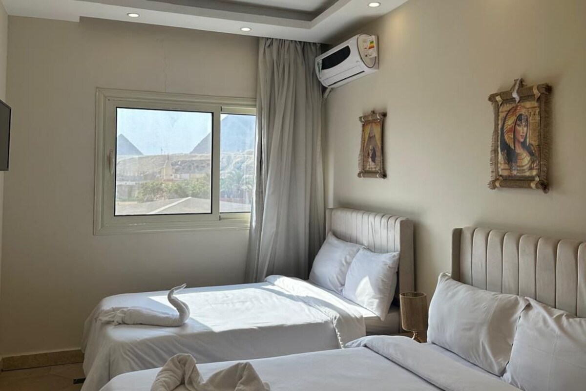 Une chambre d’hôtel avec deux lits, une grande fenêtre, un climatiseur et un tableau au mur.