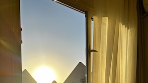 A room with a bed and a window overlooking a pyramid at sunset. - Pyramids Era View (Giza)